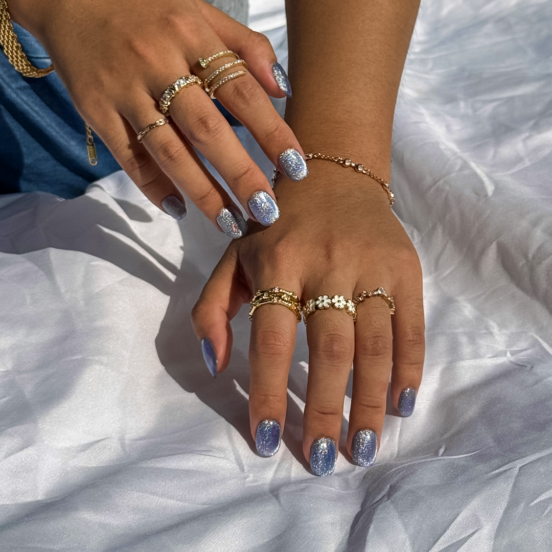 Fincloset Blue Lace cat-eye press on nails in short round shape, chic and trendy artificial nails styled with gold rings, summer manicure aesthetic on white fabric background.