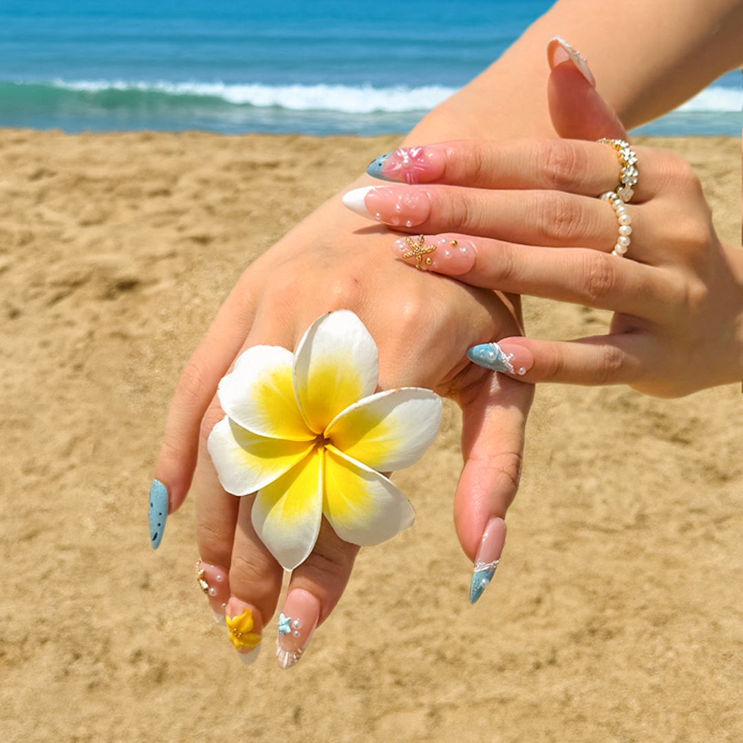 Fincloset handmade almond-shaped tropical press-on nails in white and ocean blue, detailed with plumeria flowers and gold starfish, inspired by serene island light.