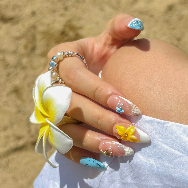 Close-up of Fincloset handmade almond shape press-on nails inspired by tropical summer island vibes, featuring 3D yellow flower, pearls, and beach-themed blue accents.