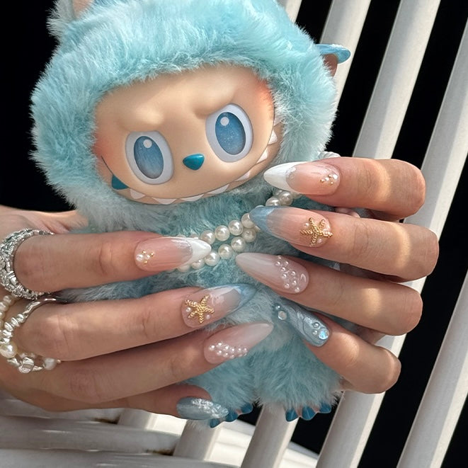 Seanova ocean-inspired press on nails from Fincloset, featuring starfish and pearl accents in almond shape, held with cute Labubu doll – perfect for summer nail aesthetics.