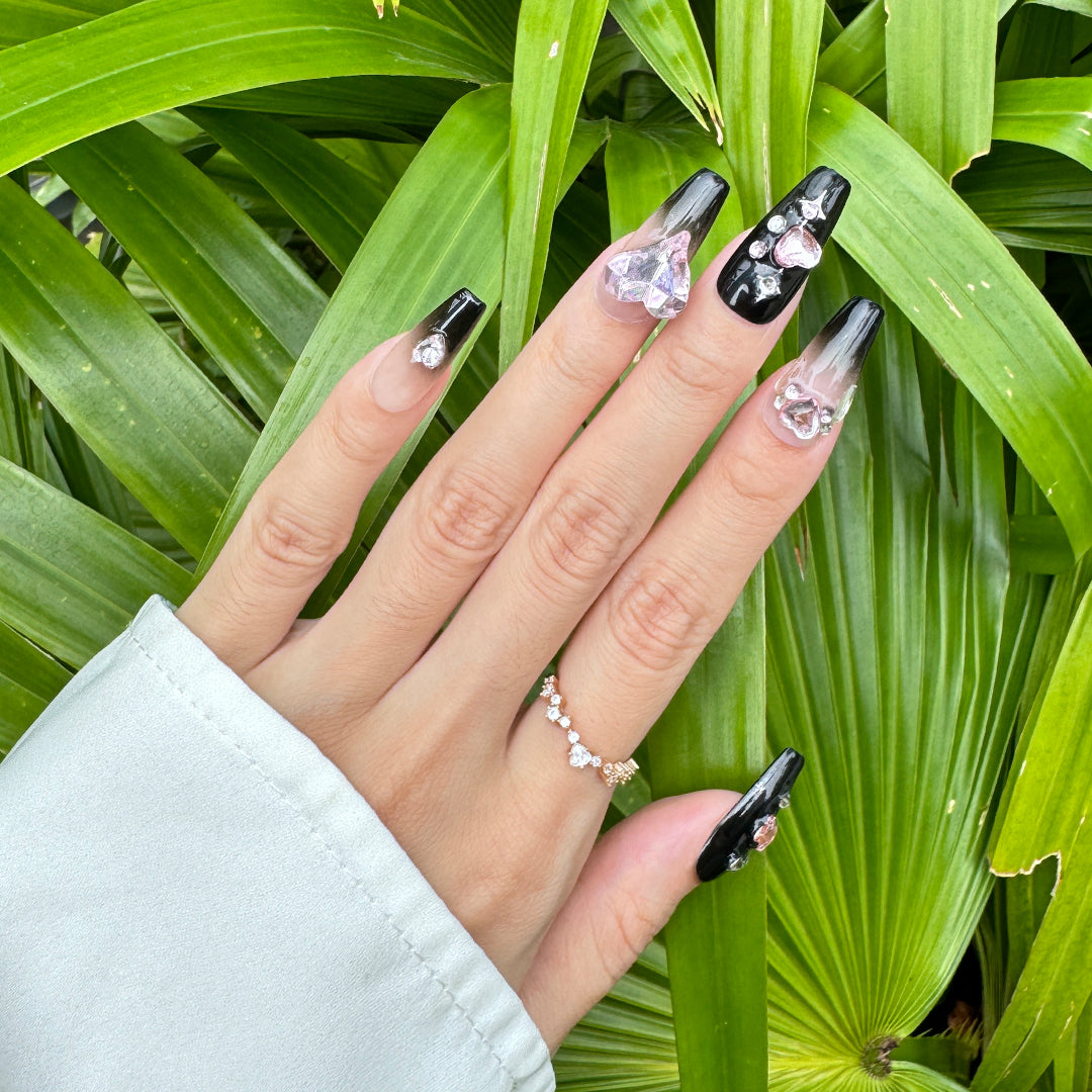 Handcrafted coffin-shaped press-on nails with black gradients, pink heart and butterfly gems, rhinestones, and star accents. Sweet, edgy, and playful.