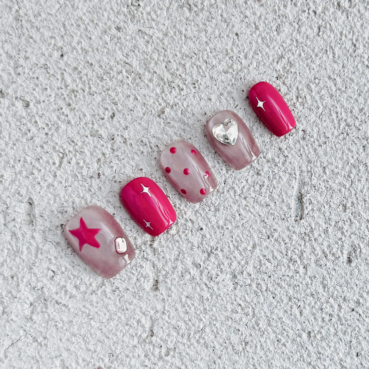 Handcrafted short square-shaped press-on nails in rosy smokey pink with soft pink cat-eye accents, featuring polka dots, stars, and diamond details for a sweet, playful, and charming style.