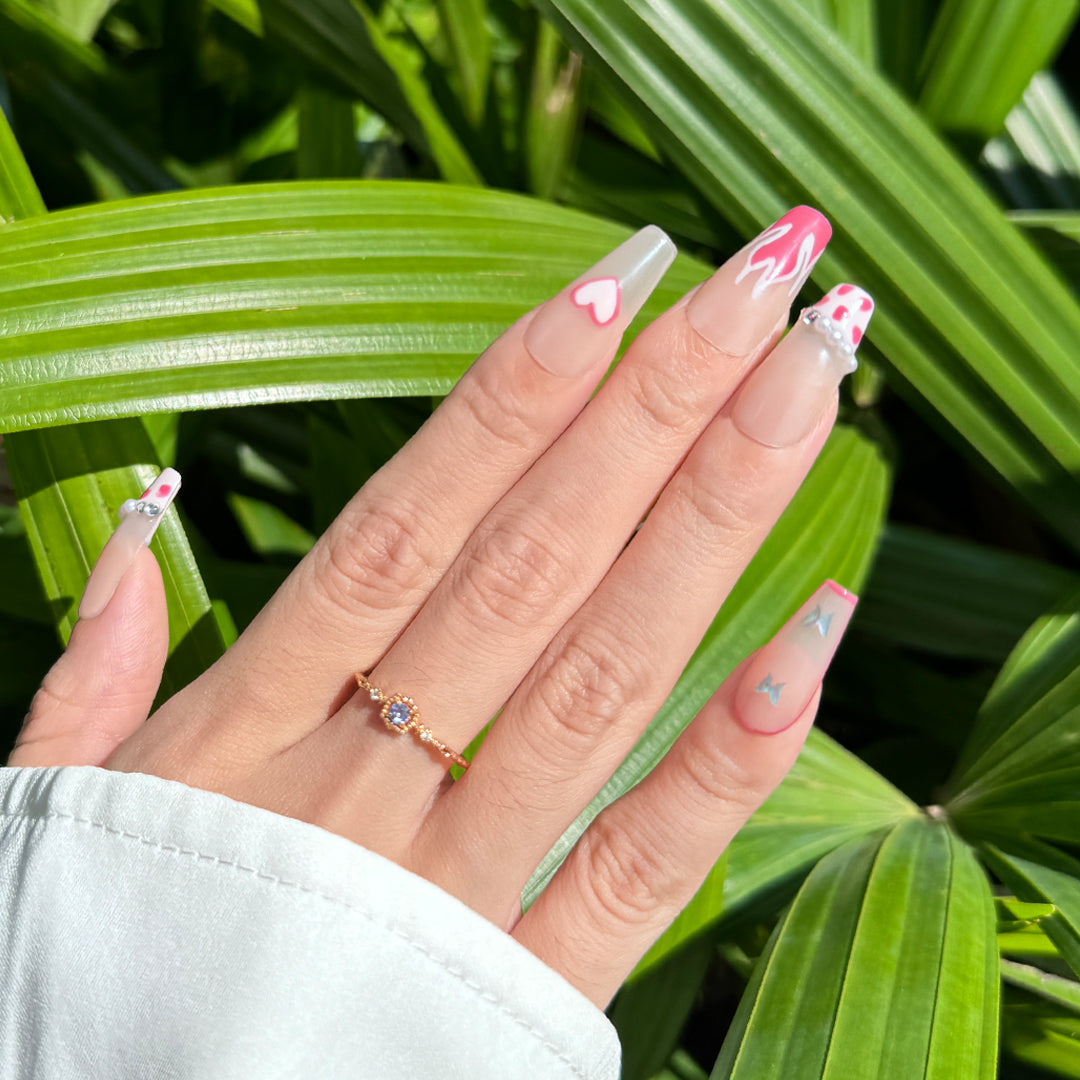 Handcrafted coffin-shaped press-on nails with translucent nude base, pink cow print, flame, heart designs, and pearl accents. Cute, playful, and elegant style.