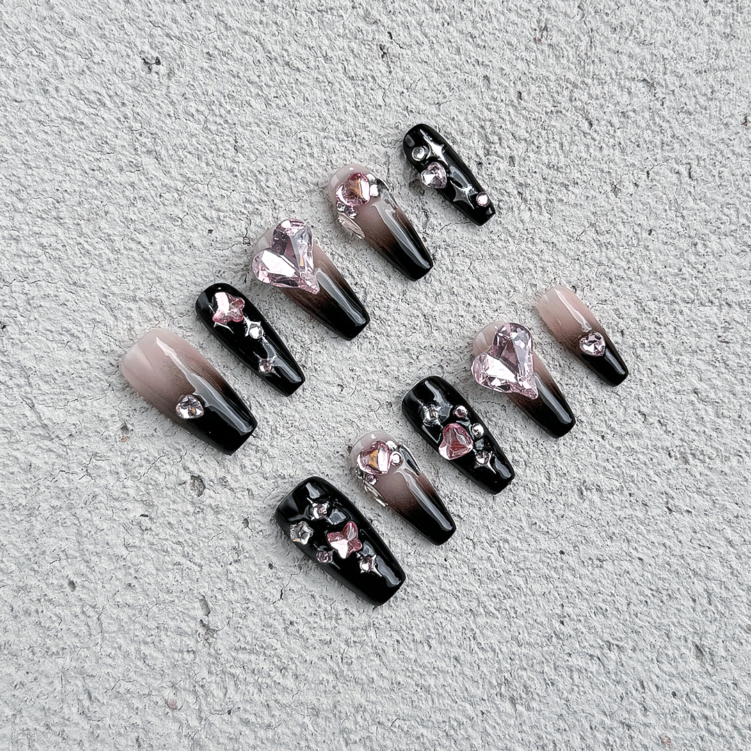 Handcrafted coffin-shaped press-on nails with black gradients, pink heart and butterfly gems, rhinestones, and star accents. Sweet, edgy, and playful.