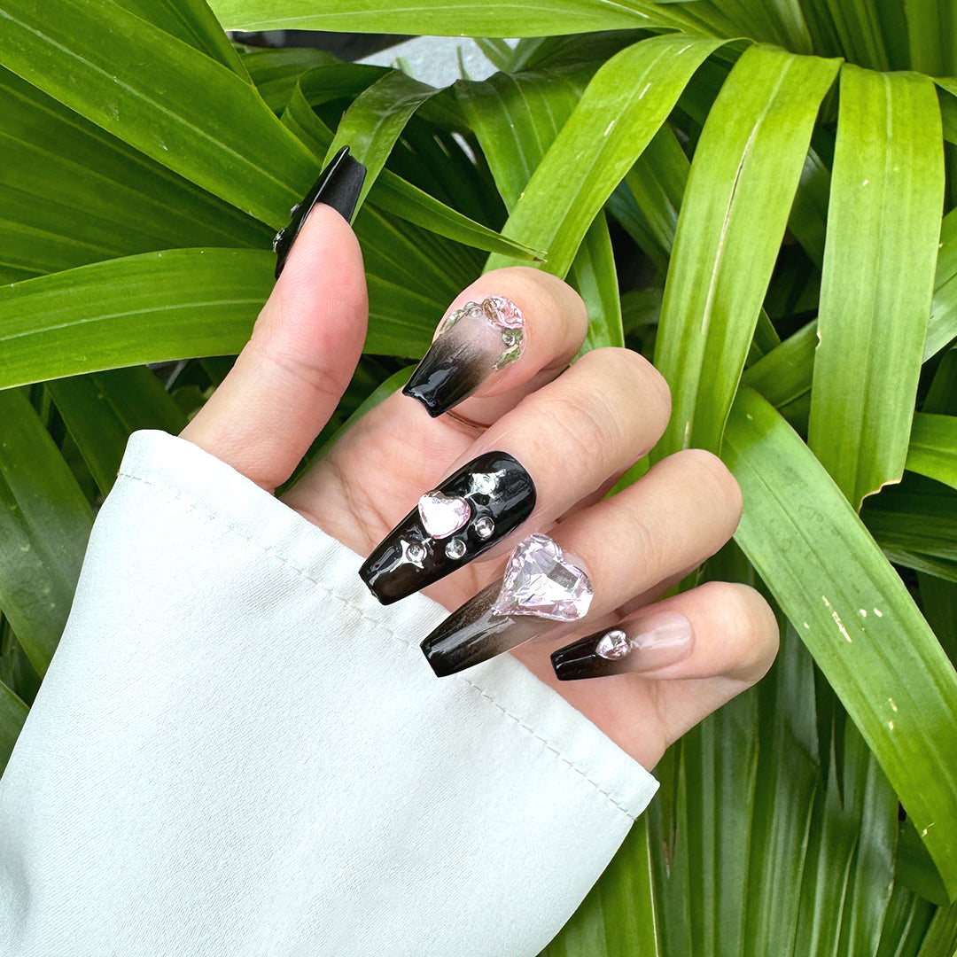 Handcrafted coffin-shaped press-on nails with black gradients, pink heart and butterfly gems, rhinestones, and star accents. Sweet, edgy, and playful.