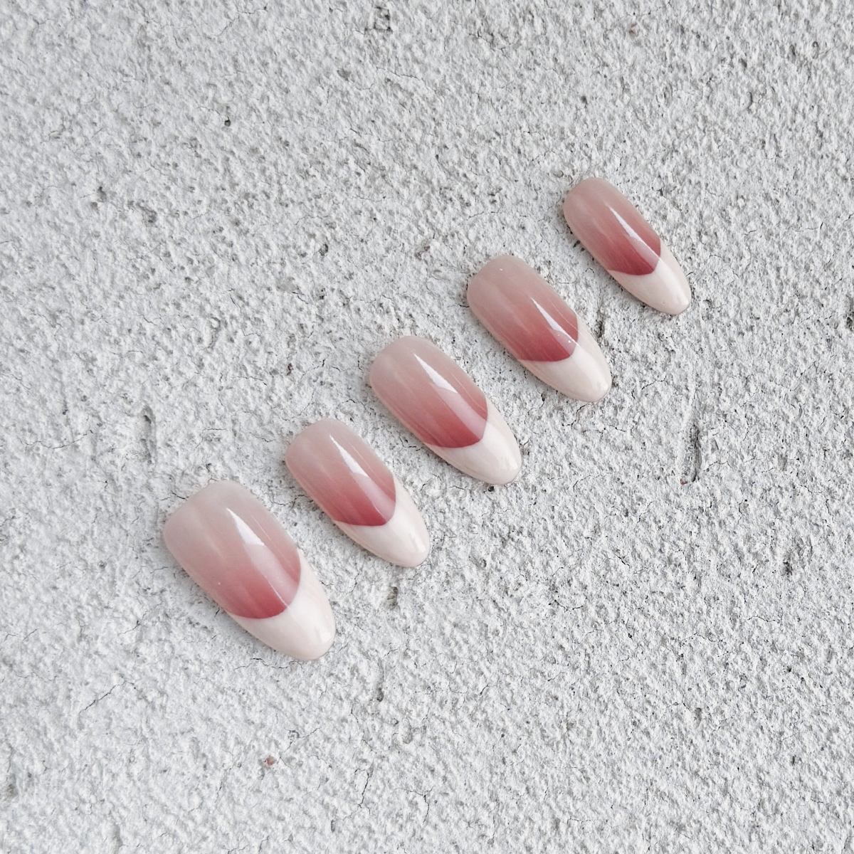 Handmade almond-shaped press-on nails with glossy nude-pink gradient French tips, offering a soft, elegant, and minimalist style.