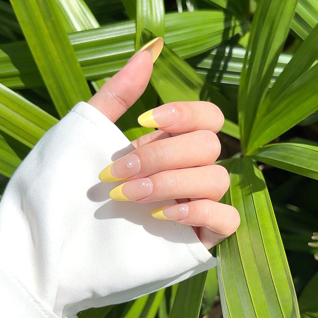 Handmade almond-shaped press-on nails with soft yellow French tips and delicate pearl accents, exuding elegance and simplicity.