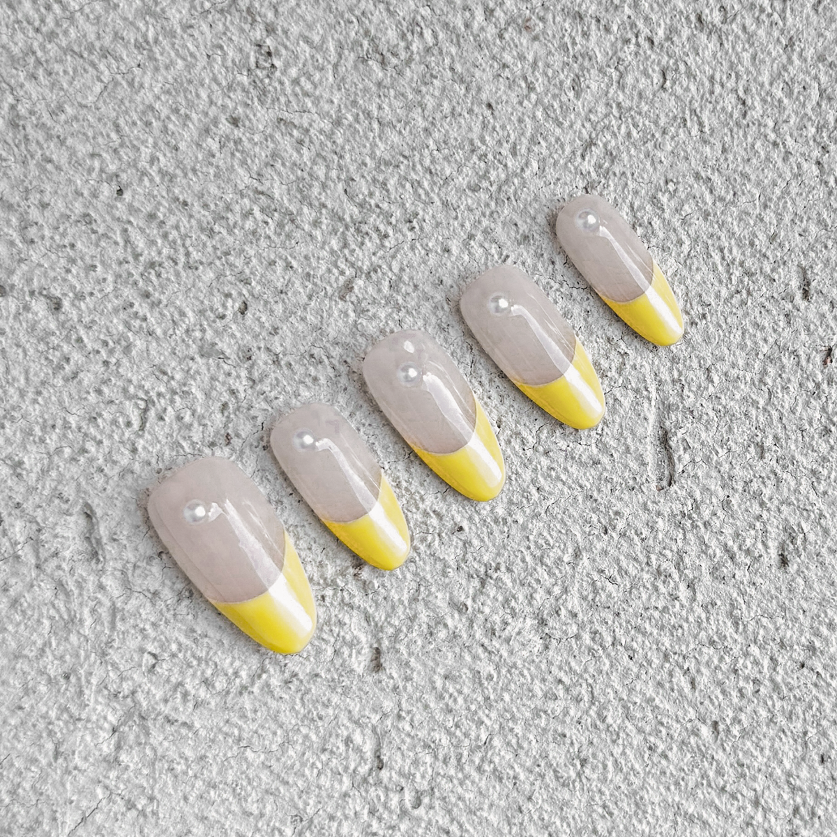 Handmade almond-shaped press-on nails with soft yellow French tips and delicate pearl accents, exuding elegance and simplicity.