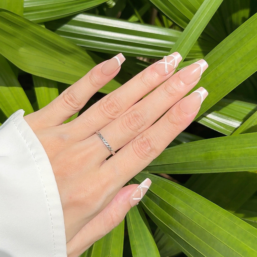 Handmade coffin-shaped press-on nails with a translucent nude base, satin pink French tips, and white ribbon-like crisscross details, inspired by ballet shoes.