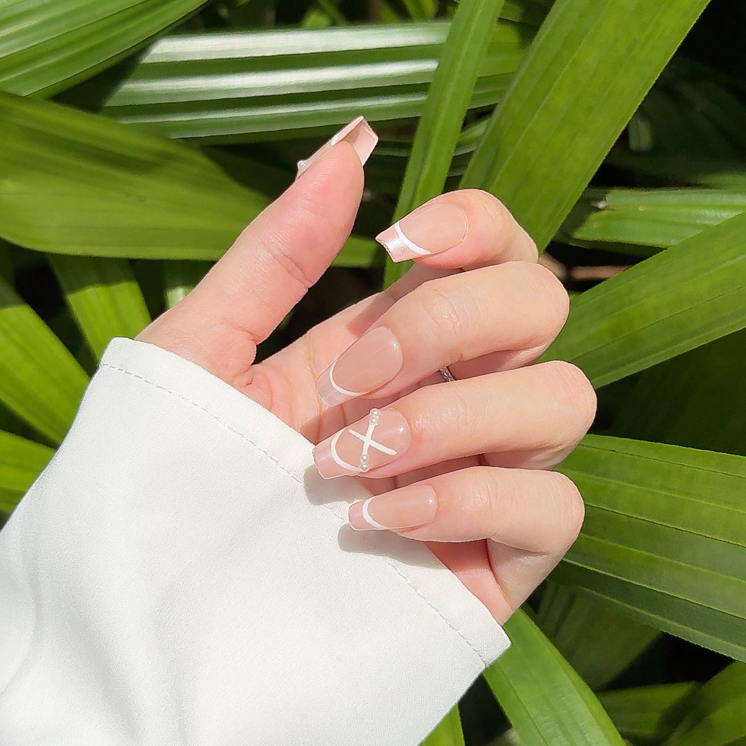 Handmade coffin-shaped press-on nails with a translucent nude base, satin pink French tips, and white ribbon-like crisscross details, inspired by ballet shoes.