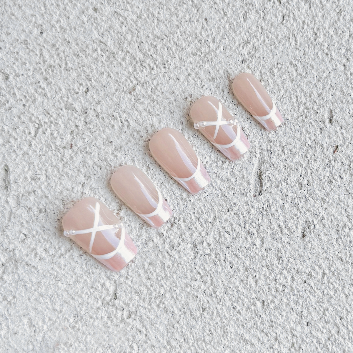 Handmade coffin-shaped press-on nails with a translucent nude base, satin pink French tips, and white ribbon-like crisscross details, inspired by ballet shoes.