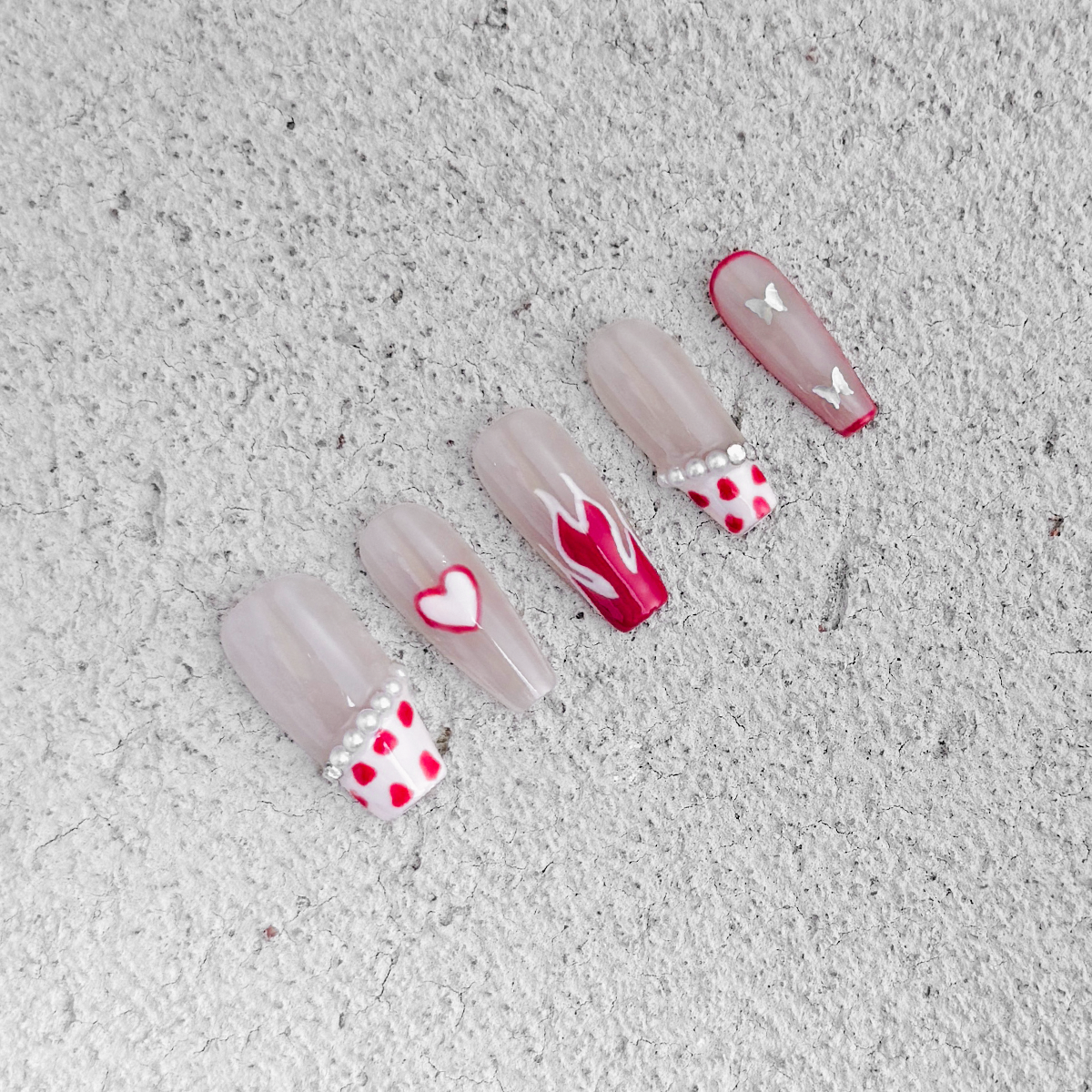 Handcrafted coffin-shaped press-on nails with translucent nude base, pink cow print, flame, heart designs, and pearl accents. Cute, playful, and elegant style.