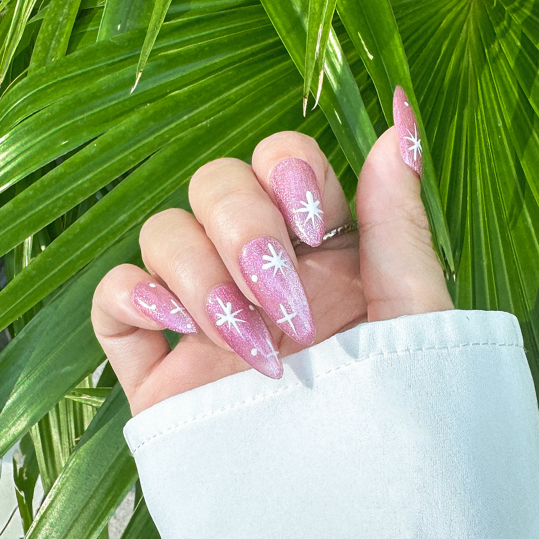 Almond-shaped press-on nails in party pink with shimmering cat-eye finish and twinkling four-point star designs. Perfect for parties and festive occasions.