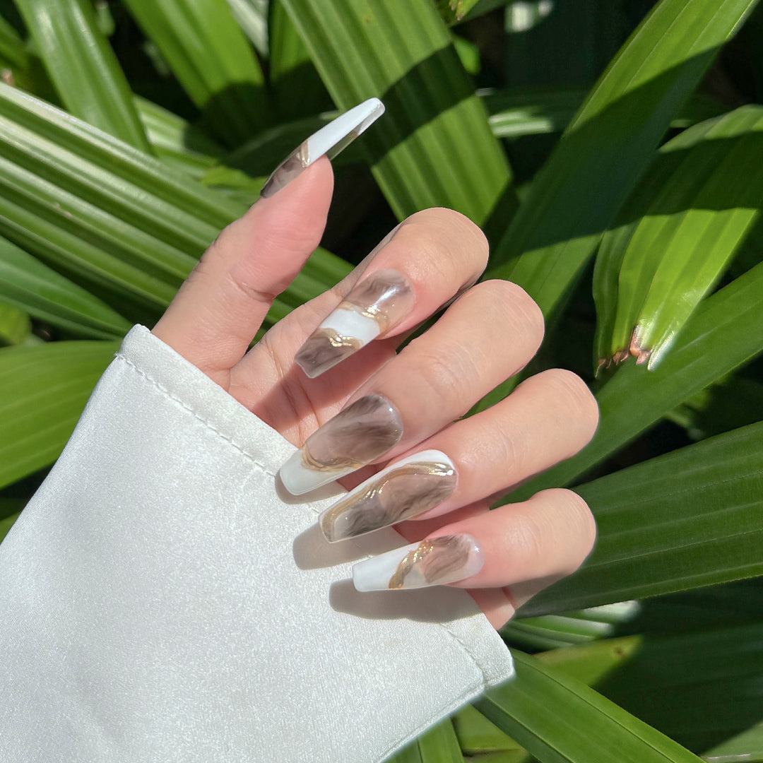 Handmade long coffin-shaped press-on nails with marble patterns and gold brushstroke accents, minimalist and elegant style