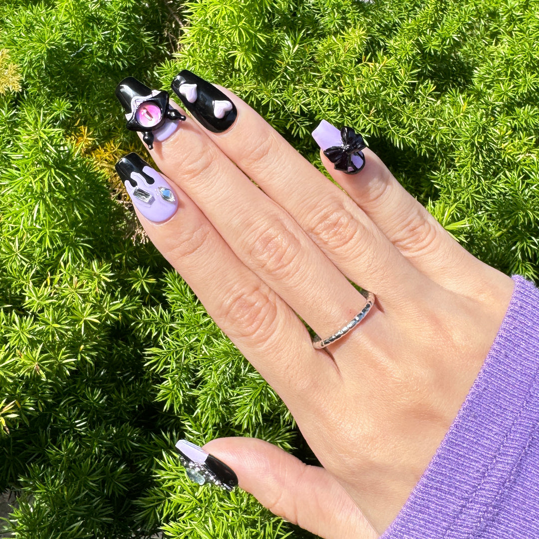 Handmade coffin-shaped press-on nails in black and candy purple with 3D devil eye decorations, offering a playful, sweet, and edgy style.